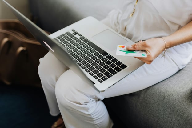 Woman sitting on couch with her laptop on her lap, holding a credit card to shop online